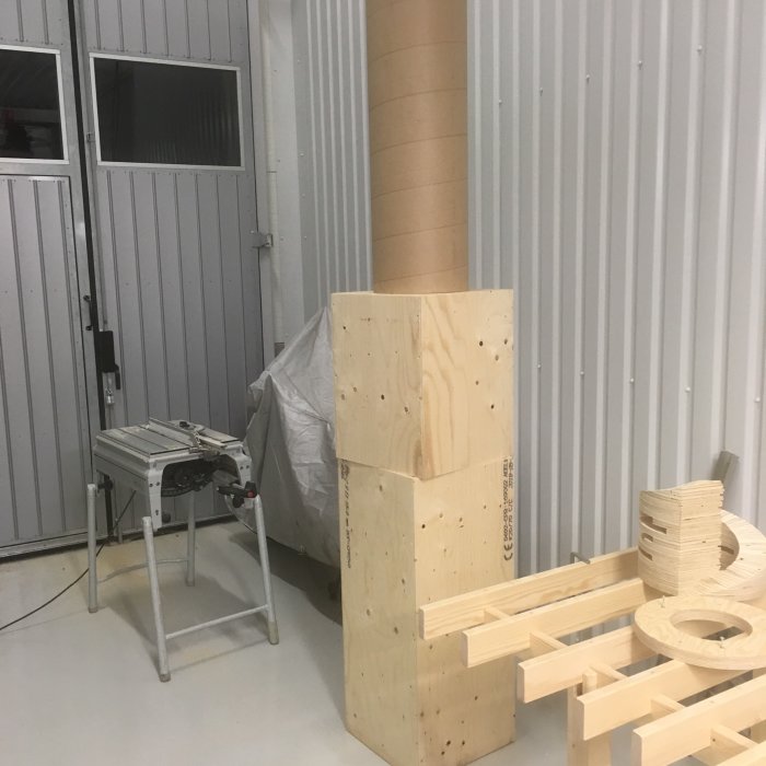 Verkstadsinredning med träkomponenter och kartongrör, arbetsbänk och täckt redskap i bakgrunden.