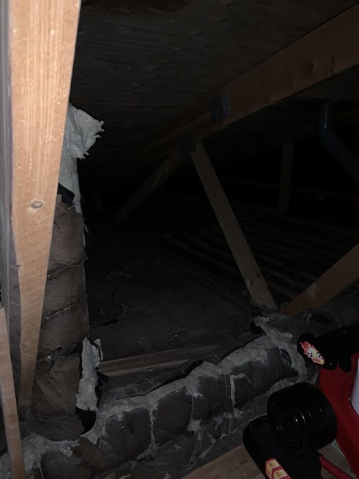 Mörk vind med synliga träbjälkar och isoleringsmaterial, inga VVS-installationer synliga.