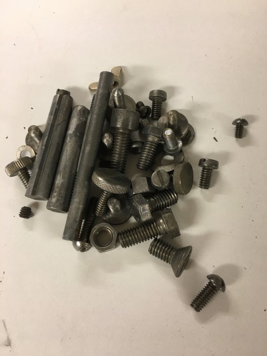 Hög av blandade metallbultar och skruvar på en vit yta.