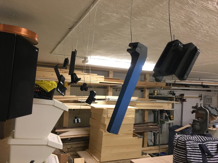 Målade föremål hänger på trådar i en verkstad, nyss sprayade med hammarlack.