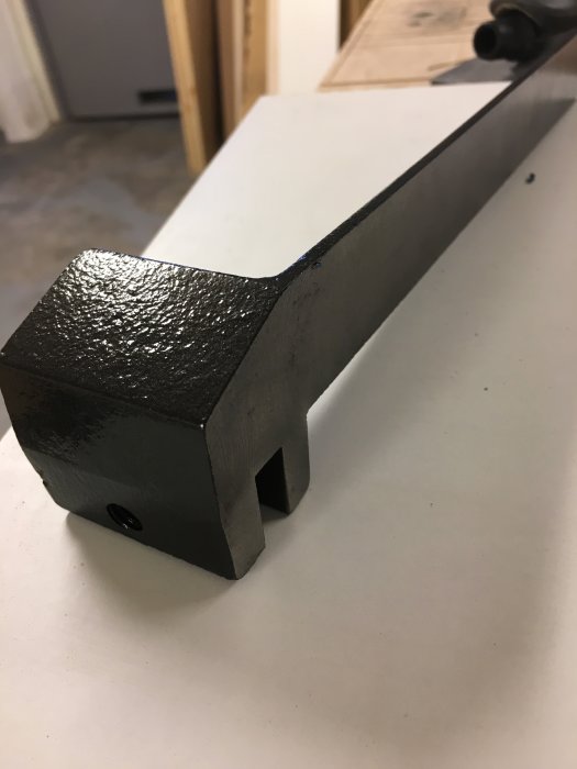 Verktygsdel målat med hammarlack, svart strukturfärg och skarpa kanter, på en vit bänk.