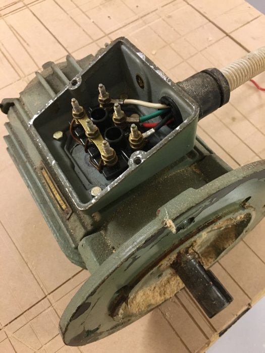 En demonterad maskindel med synliga kablar och anslutningar, rost och smuts intill hjulet som ska renoveras.