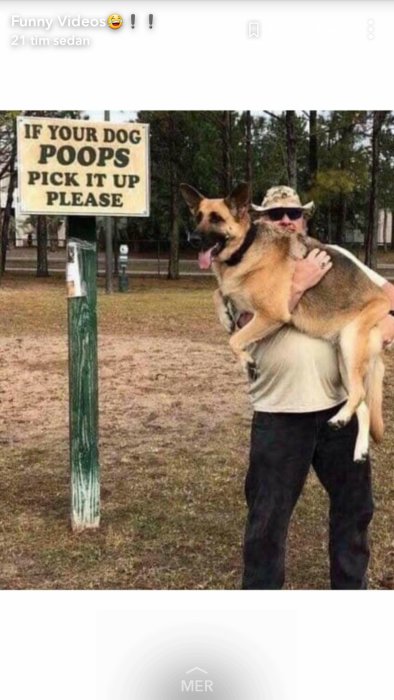 Person bär på stor schäfer framför skylt med text "If your dog poops pick it up please".