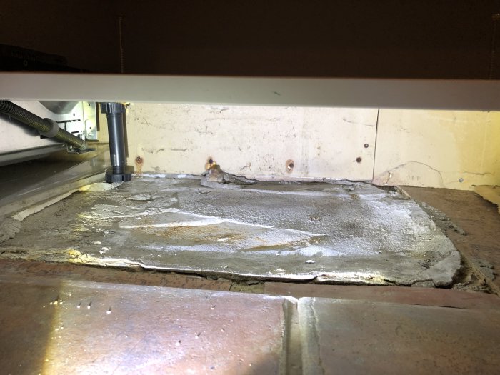 Vy under köksskåp med synliga glipor mellan golvreglar och gjuten golv.