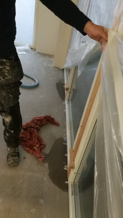 Person drar bort skyddsplast i rum med renoveringsarbete, färg spilld på golv.