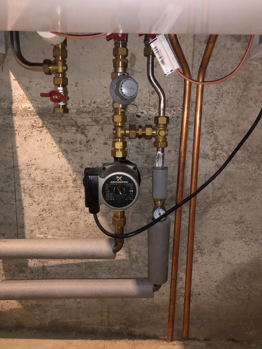 Värmesystem med cirkulationspump, shunt och termostat på returledningen i en källare.