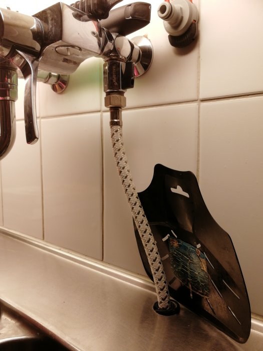 Kökshandfat med en blandare och improviserad installation av slangar och en mellankoppling.