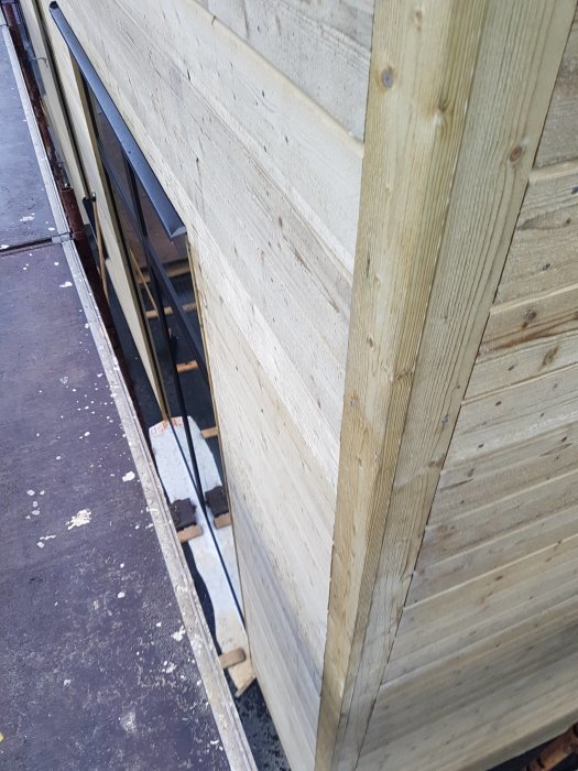 Nybyggd träpanelvägg med hörnfönster och monterad ränna från Lindab på byggställning.