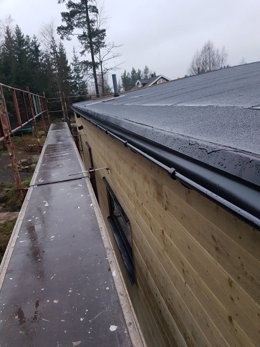 Takränna monterad på en byggnad med synlig träpanel och hörnfönster, omgivet av byggställningar och frostat tak.