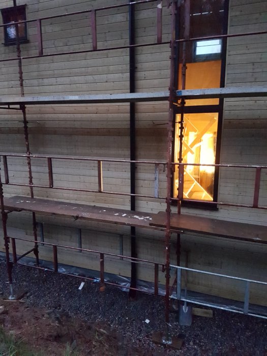 Nybyggt hörnfönster på hus med träpanel och byggnadsställning vid skymning.