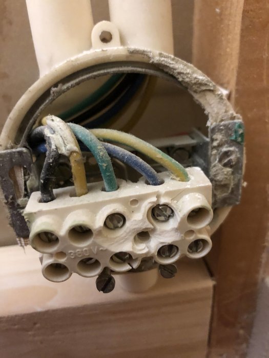 Eluttag utan kåpa med synliga kablar och anslutna trådar i en vägg under installation.