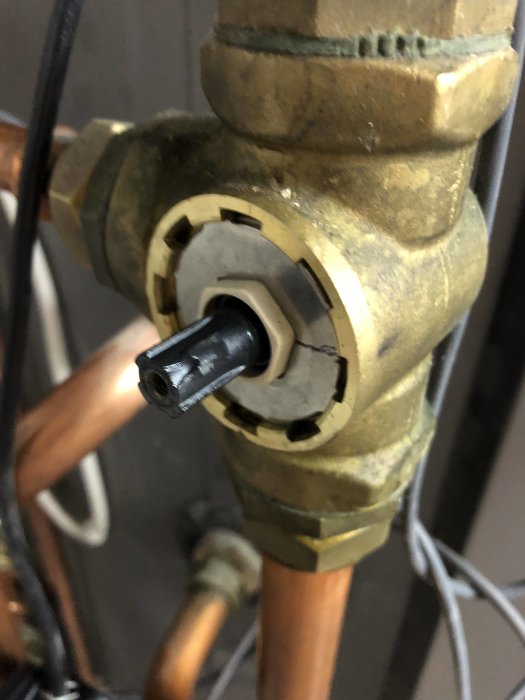 Någon håller i en shunt motor monterad på en shuntventil med kopparledningar synliga, tänkt för värme/vattenflöde.