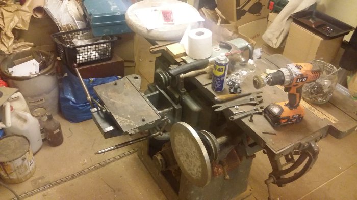 En arbetsbänk med gammal kombimaskin och verktyg, inklusive borr och WD-40, i ett rörigt snickerirum.