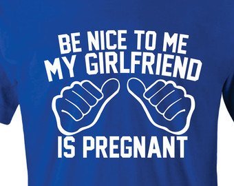 Blå t-shirt med texten "BE NICE TO ME MY GIRLFRIEND IS PREGNANT" och två illustrerade knutna händer.