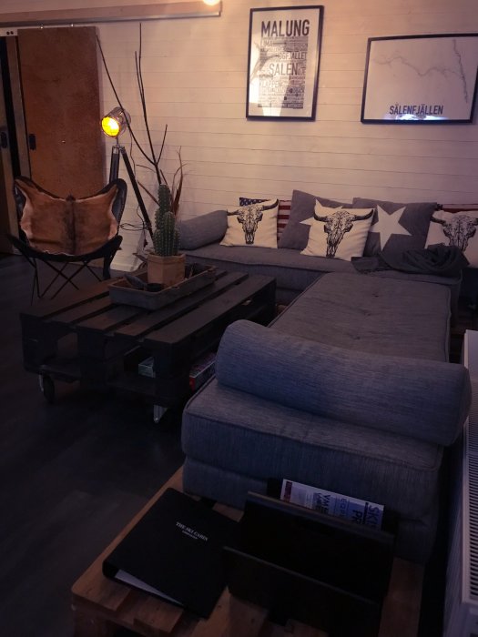 Ett mysigt vardagsrum med soffa, kuddar, träbord, växt och en lampa på stativ, inrett i varma färger.