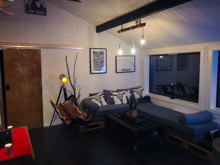 Vardagsrum under renovering med soffa, fåtölj och tavlor på väggen, mysig belysning.