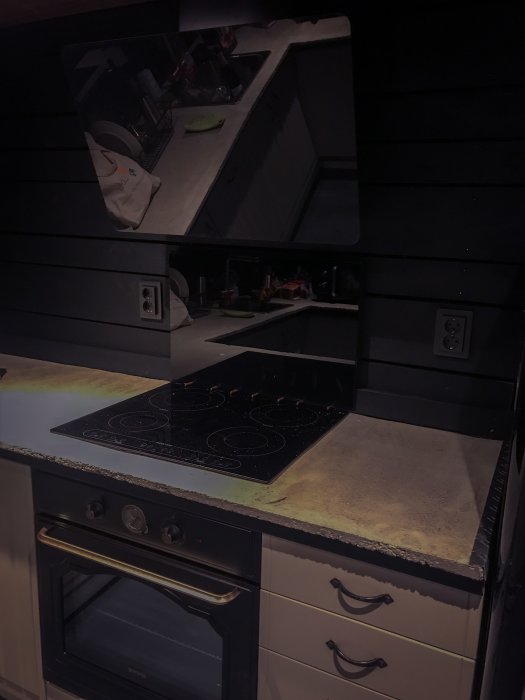 Mörkt kök med nyinstallerad fläkt och stänkskiva bakom spishäll och ugn.