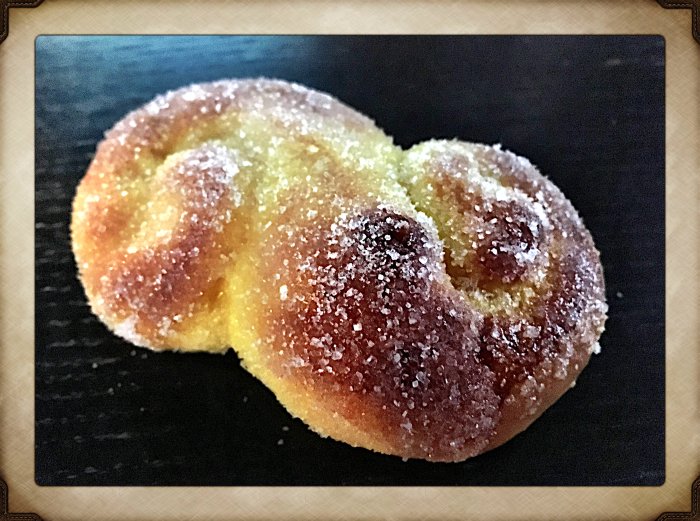 Nybakad lussebulle med saffran och sockerströssel på ett mörkt underlag.