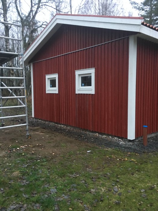 Rödmålad byggnad nästan färdigställd med plankor och spont, två fönster installerade, byggnadsställning bredvid.