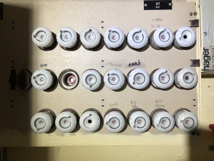 Elcentral med säkringar och handskrivna etiketter på en vägg.