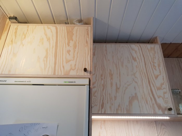 Furuplywood behandlad med Osmo Snö och ofärgad matt finish, monterad som takskåpsdörrar över en diskmaskin.