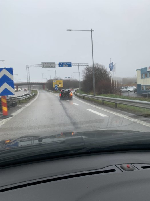 Bil som transporterar långt föremål utan släp på motorvägen under grå himmel.