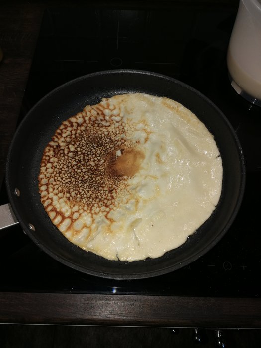 Stekpanna på induktionshäll med pannkaka som är ojämnt gräddad, varmare och mörkare på ena sidan.