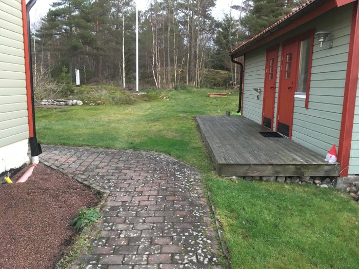 Trädgård vid huvudbyggnad med grus, gräsmatta, altan och stig, potentiellt för byggprojekt.