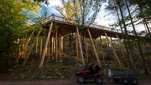 Trädeck på stöttor i skogsområde med ATV-fordon som passerar nedanför.