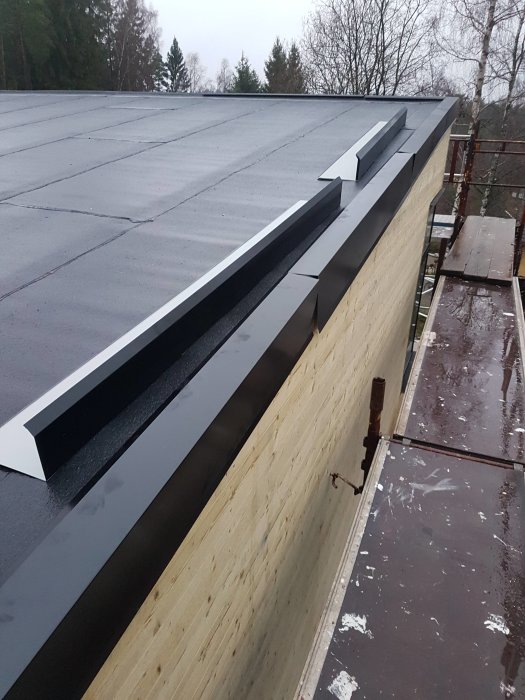 Nyinstallerad kröningsplåt längs husets takkant med ställning synlig nedanför.