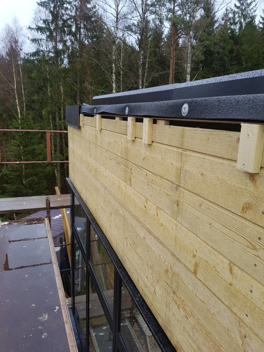 Monterad kröningsplåt längs trävägg på byggnad med synliga distansklossar och ställning i bakgrunden.