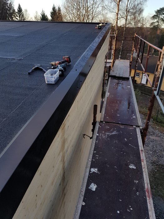 Nyinstallerad kröningsplåt på takkant med verktyg, distansklossar och del av byggställning.