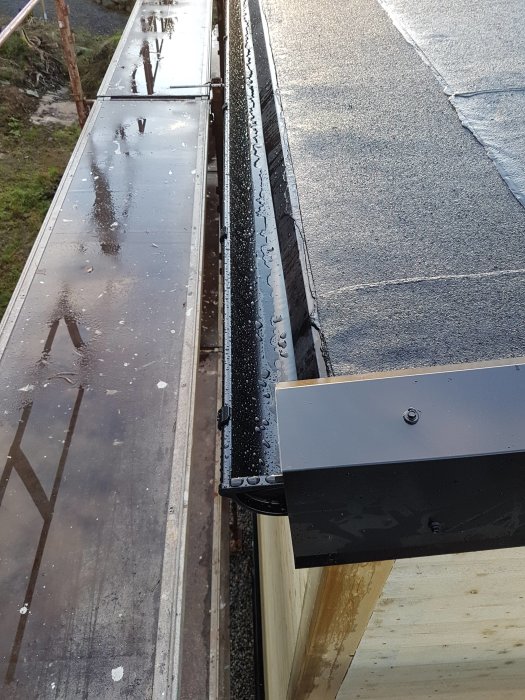 Närbild på nyinstallerad kröningsplåt längs takkanten, med distansklossar för luftning, ovan en svart takpapp.