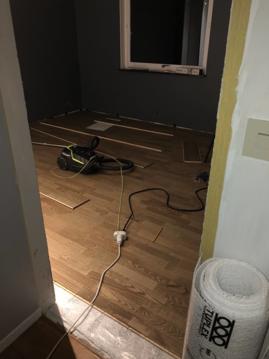Pågående läggning av laminatgolv i rum med verktyg och elsladdar på golvet.