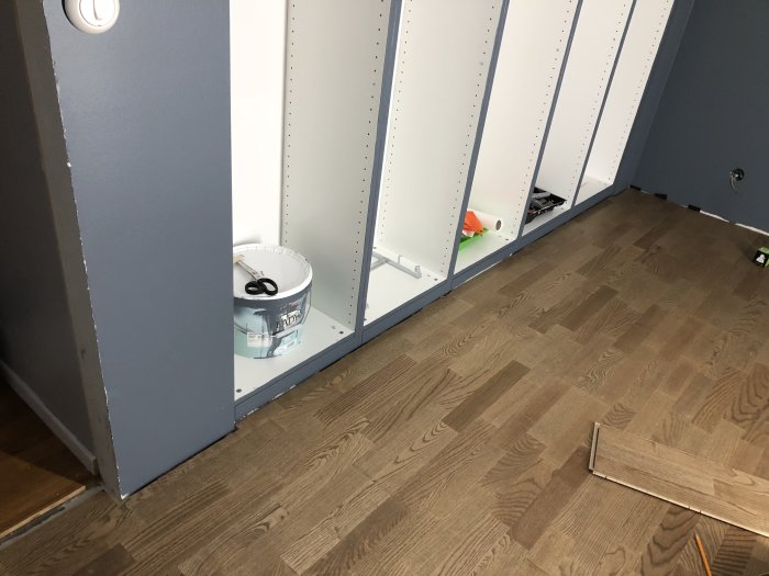 Nylagt asklaminatgolv med öppna vita garderober och golvplankor som skall läggas.