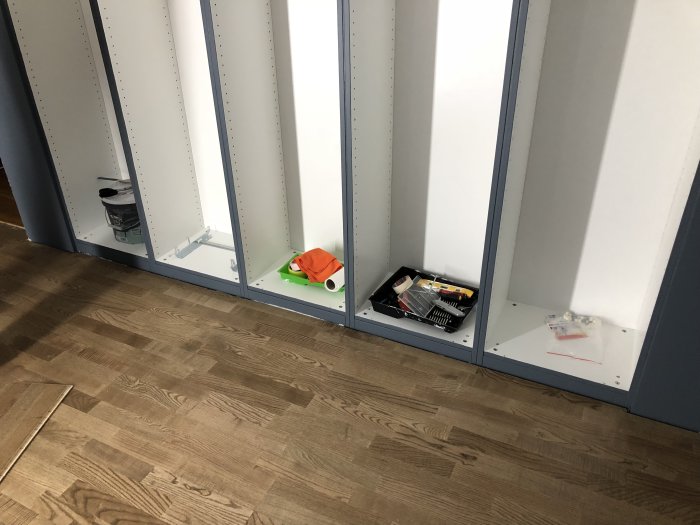 Delvis lagt asklaminatgolv med byggmaterial och verktyg synliga vid icke monterade skåpelement.
