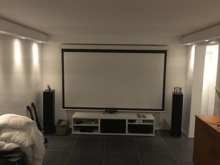 Ett tv-rum med projektorvägg, högtalare, möbler och LED-nisch i taket.