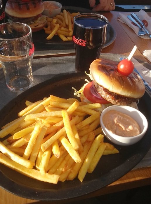 Hamburgare med pommes frites, sås och en Coca-Cola-glas på ett serveringsfat.