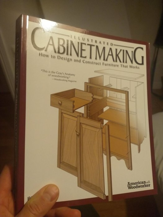Hand håller en bok med titeln "Illustrated Cabinetmaking" om design och konstruktion av möbler.