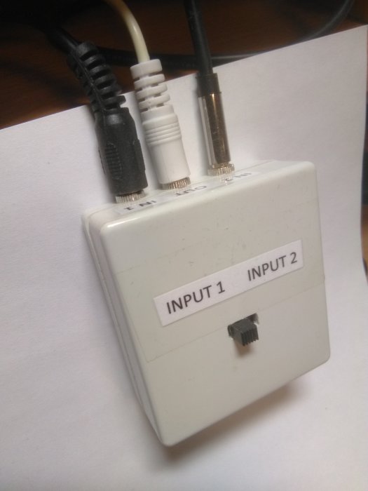DIY omkopplare med tre 3.5mm ljuduttag märkta "INPUT 1" och "INPUT 2" med anslutna kablar.