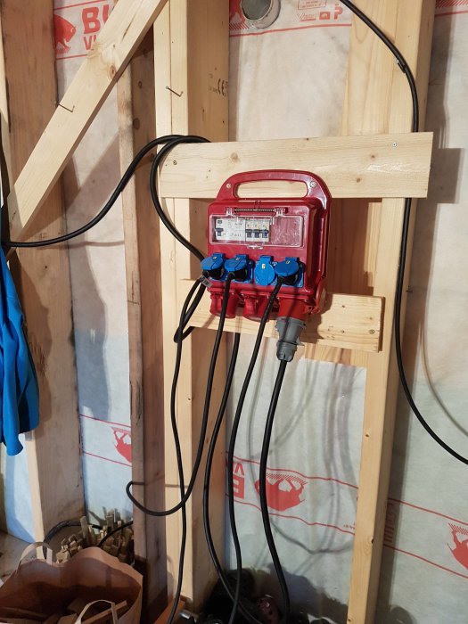 En byggcentral med anslutna kablar monterad på trästomme inne i en byggnad under konstruktion.