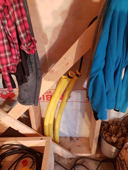 Byggarbetsplats med arbetshängda kläder, gula trefaskablar och isoleringsmaterial i bakgrunden.