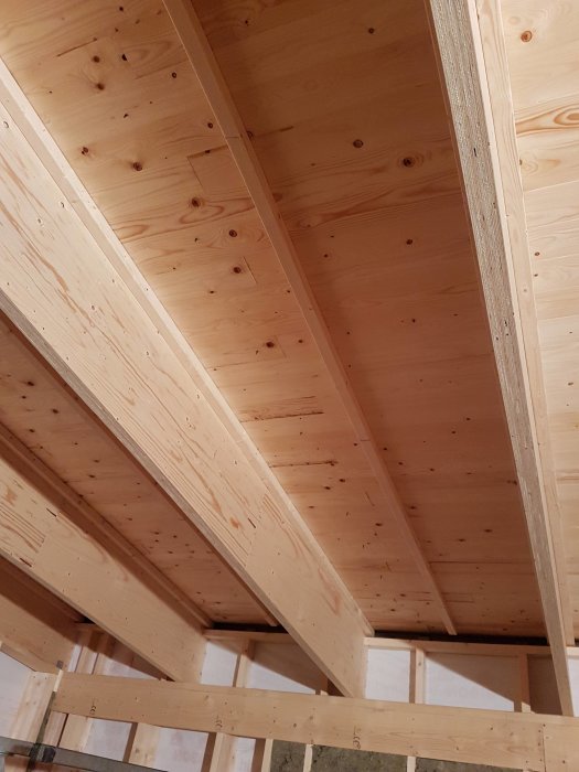 Invändig vy av träbjälklag i ett byggprojekt, oisolerad takkonstruktion av trä bjälkar och reglar.