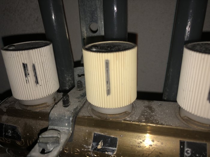 Vita radiatorventilkranar och reglage på en dammig yta, person söker hjälp för att demontera.