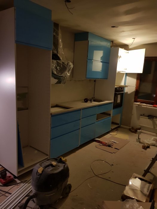 Omonterat kök med blåfärgade lådor och skåpluckor, med belysning installerad och byggverktyg på golvet.