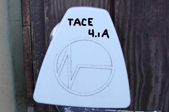 Vit ställdon med texten "TACE 4.1A" mot en trädvägg.