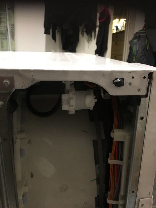 Öppen tvättmaskin som visar slangar och den vita elektriska komponenten som beskrivs i inlägget.