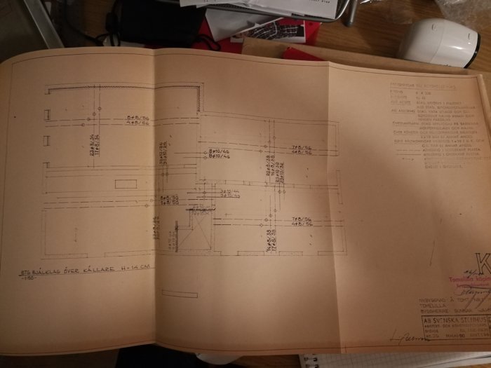 Uppslagen arkitektritning på bord visande detaljer för byggprojekt inklusive mått på betongvalv.