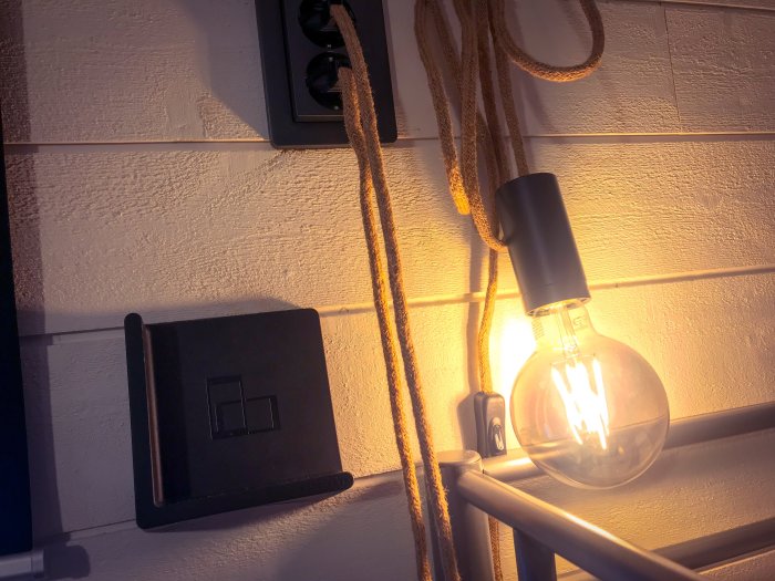 Närbild av tänd glödlampa med rep som en del av inredningen i en nyklar skidstuga.