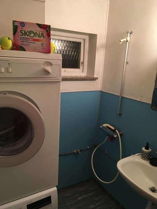 Före-renovering av badrum med ljusblå väggar, gammal duschblandare och vit tvättmaskin.